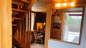 L’intérieur d’un chalet en bois, avec un escalier, un fauteuil à bascule en bois, une petite table et une fenêtre donnant sur l’extérieur.
