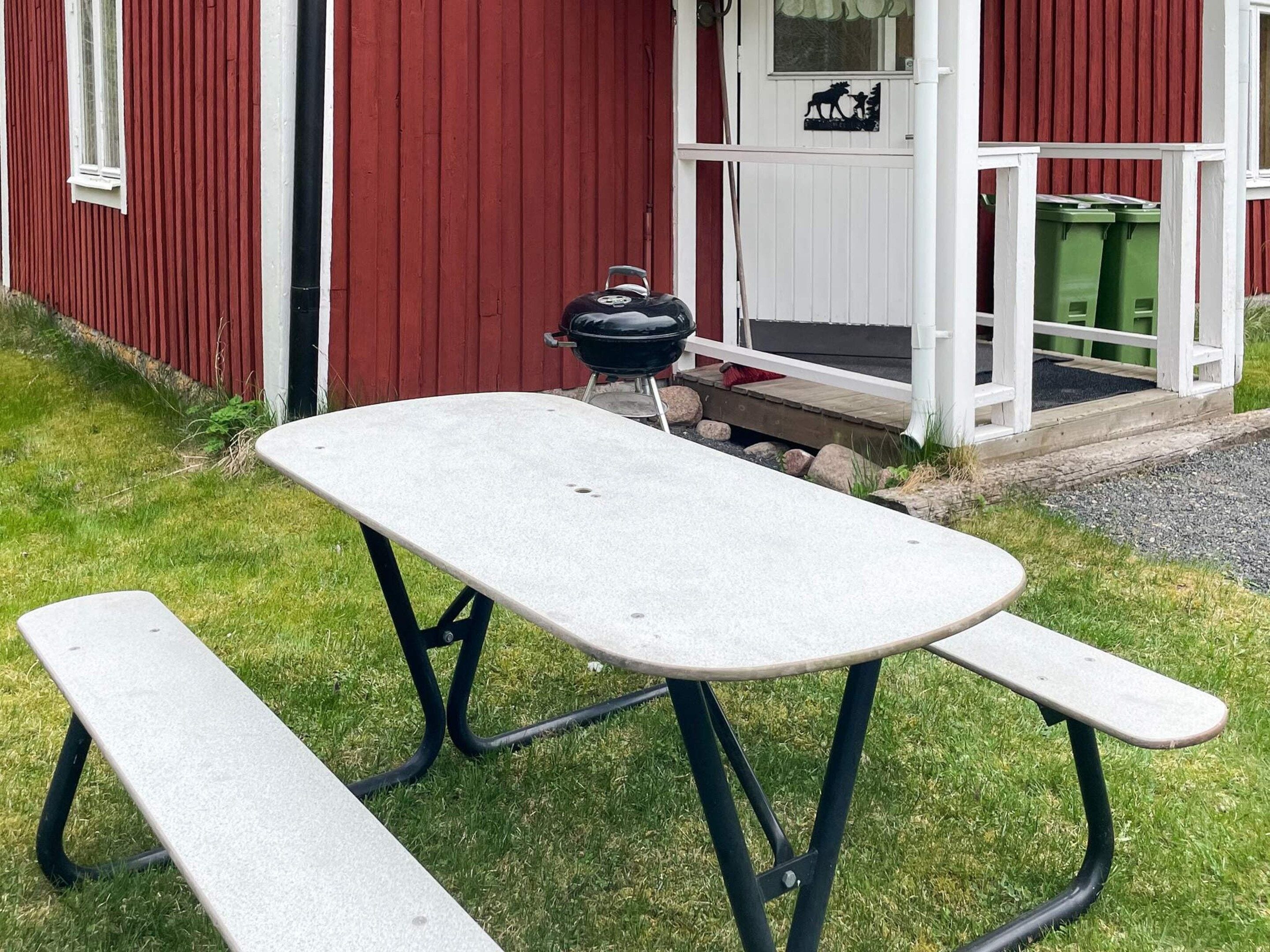 A picnic table with benches in front of a red building with a white door and a window.