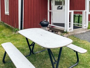 A picnic table with benches in front of a red building with a white door and a window. - 7 Person Holiday Home in Lekeryd (Lekeryd)