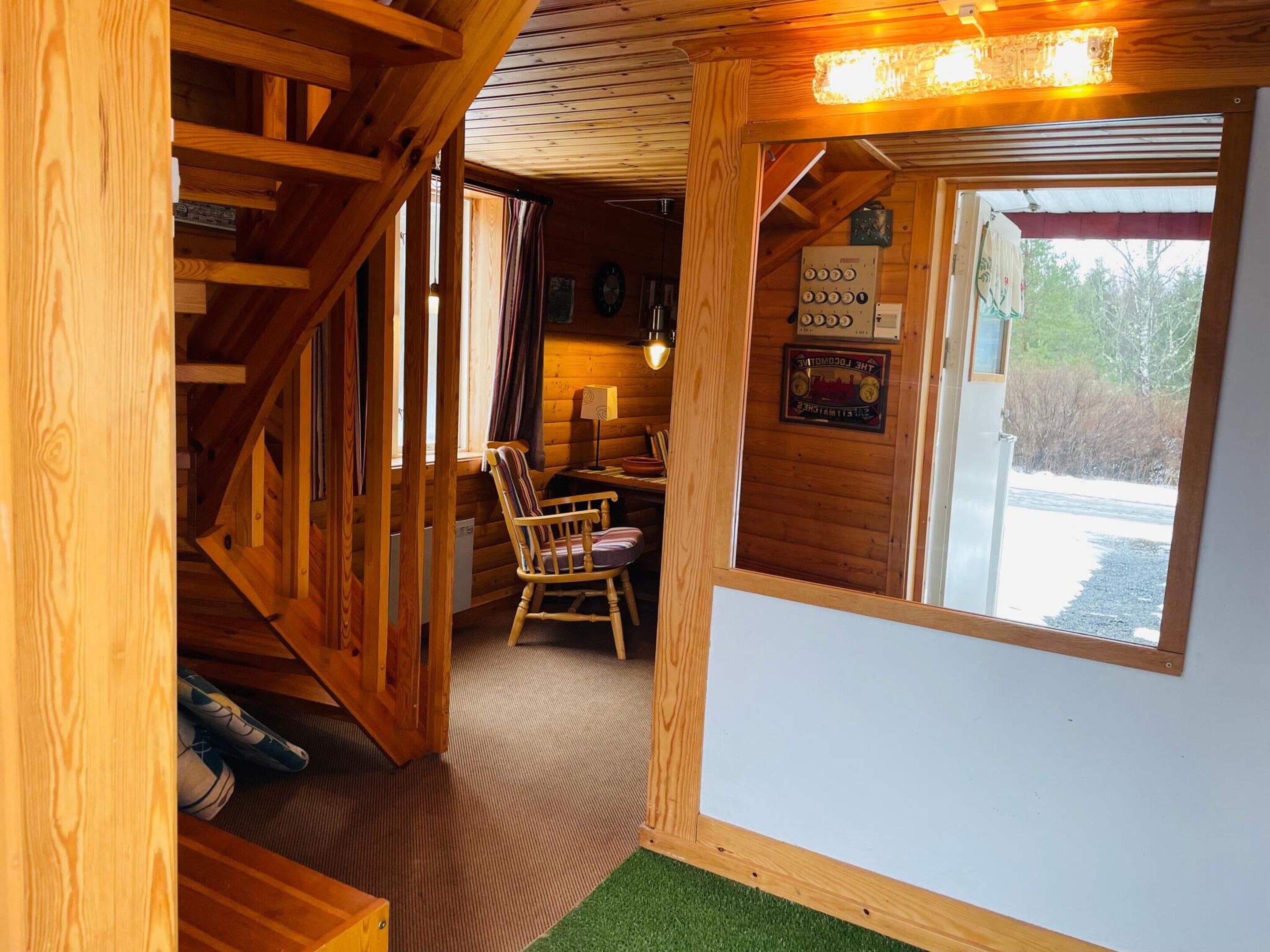 Un interior de madera con una escalera, una silla de madera, una mesa y una ventana con vistas.