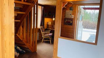 Un interior de madera con una escalera, una silla de madera, una mesa y una ventana con vistas.