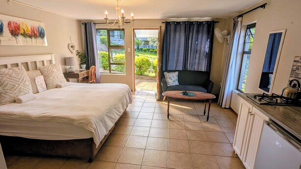 Un dormitorio con cama, escritorio, silla, sofá y vistas al jardín.