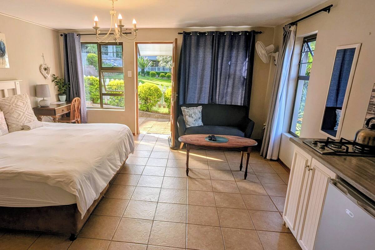 Une chambre à coucher comprenant un lit, un bureau, une chaise, un canapé et donnant sur le jardin.