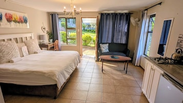 Um quarto com cama, escrivaninha, cadeira, sofá e vista para o jardim.