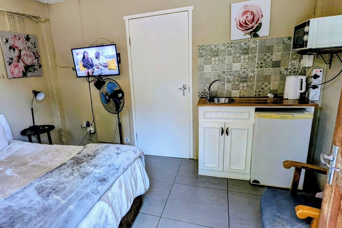 Ett litet, kompakt rum med en säng, en tv, en fläkt, ett handfat och en mikrovågsugn.