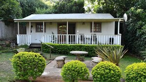 Una casa de un solo piso con un porche, rodeada de setos cuidados y un pequeño jardín con una mesa y sillas de piedra.