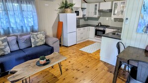 Un espacio habitable compacto con sofá, una pequeña mesa de comedor, kitchenette y piso de madera.