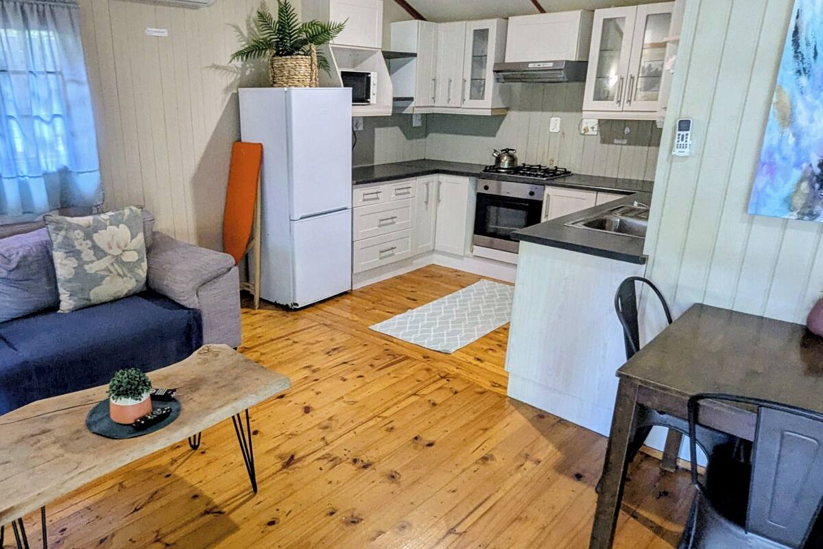 Un espace de vie compact comprenant un canapé, une petite table à manger, un coin cuisine et un plancher en bois.