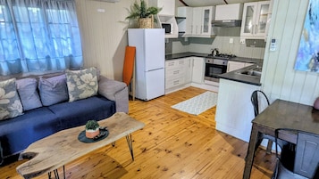 Um espaço compacto com sofá, uma pequena mesa de jantar, cozinha compacta e piso de madeira.