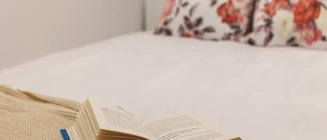 An open book on a bed with a floral pillow in the background.