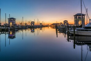 A marina with boats docked, calm water, and illuminated structures at dusk.