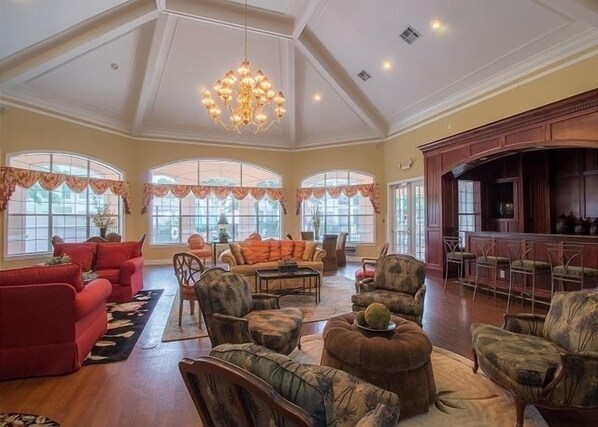 A spacious living room with a high ceiling, large windows, and a chandelier.