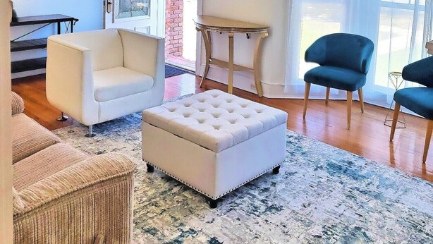 A living room with a white sofa, a blue armchair, a small round table, and a chandelier. - Charming Home on Porter Avenue! (Biloxi)