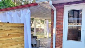 A covered patio area with a wooden fence, a brick wall, and a door with a welcome mat. - Charming Home on Porter Avenue! (Biloxi)