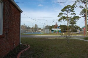 A brick building with a visible window and a fenced tennis court in the background. - Charming Home on Porter Avenue! (Biloxi)