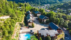 Vista aérea de un complejo turístico con varias edificaciones, una piscina y follaje circundante.