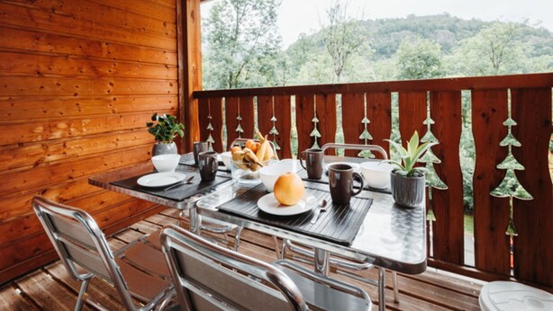 Una terraza de madera con una mesa dispuesta para el desayuno, incluyendo pan, un muffin y una taza de café.