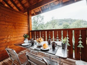 Una terraza de madera con una mesa dispuesta para el desayuno, incluyendo pan, un muffin y una taza de café.