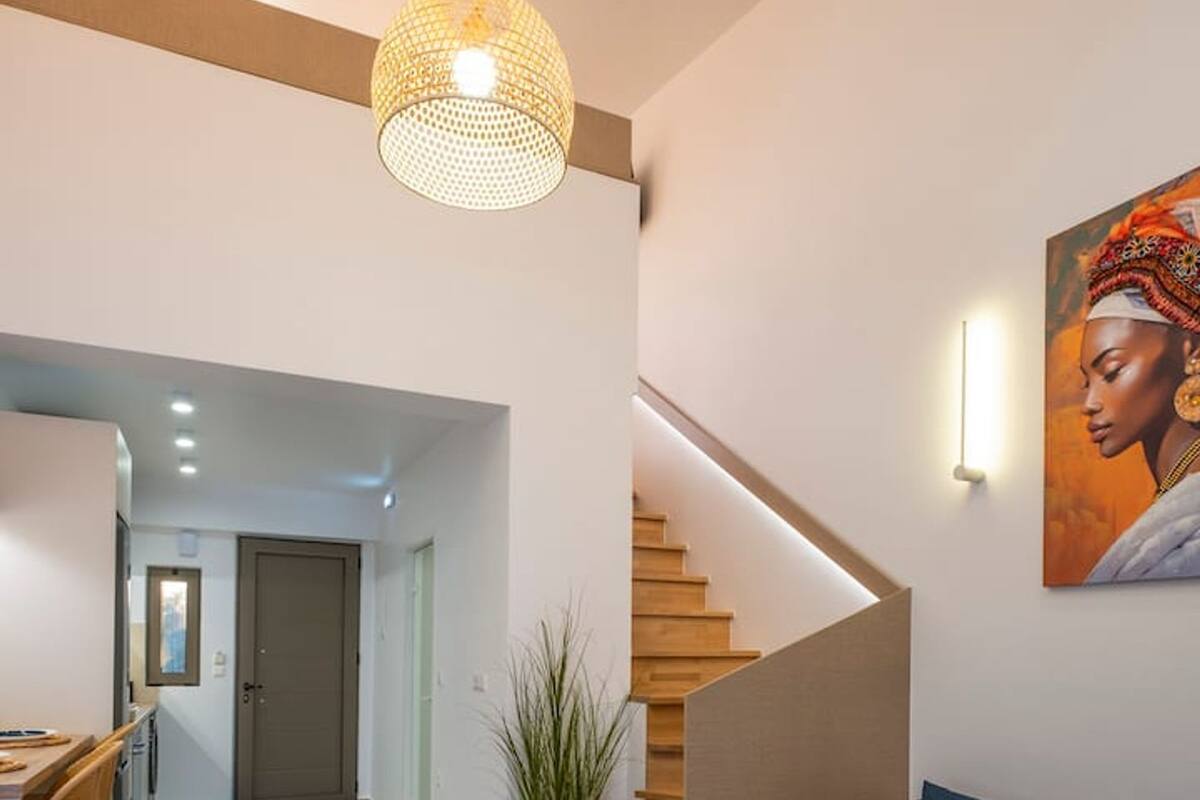 Una sala de estar moderna con un sofá azul, una mesa de centro de madera con bebidas, una escalera y un cuadro en la pared.