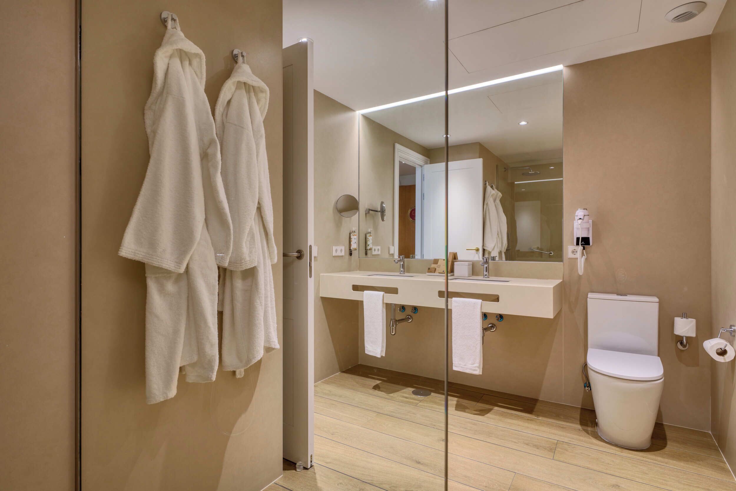 A modern bathroom with a glass shower enclosure, a double sink vanity, and a toilet.
