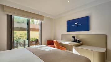 Een moderne hotelkamer met een groot bed, een bureau met stoel, een televisie en een glazen schuifdeur naar een buitenruimte.