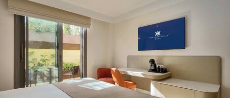 A modern hotel room with a large bed, a desk with a chair, a TV, and a sliding glass door leading to an outdoor area.