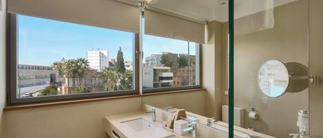A modern bathroom with dual sinks, a large mirror, and a view of the cityscape through a large window.