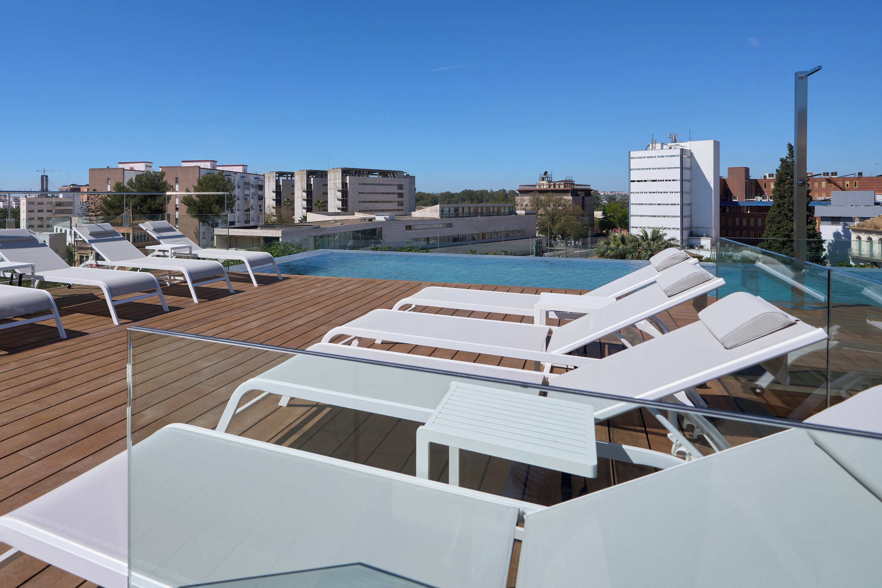 Un área de piscina en la azotea con sillones de descanso y vistas despejadas del paisaje urbano.
