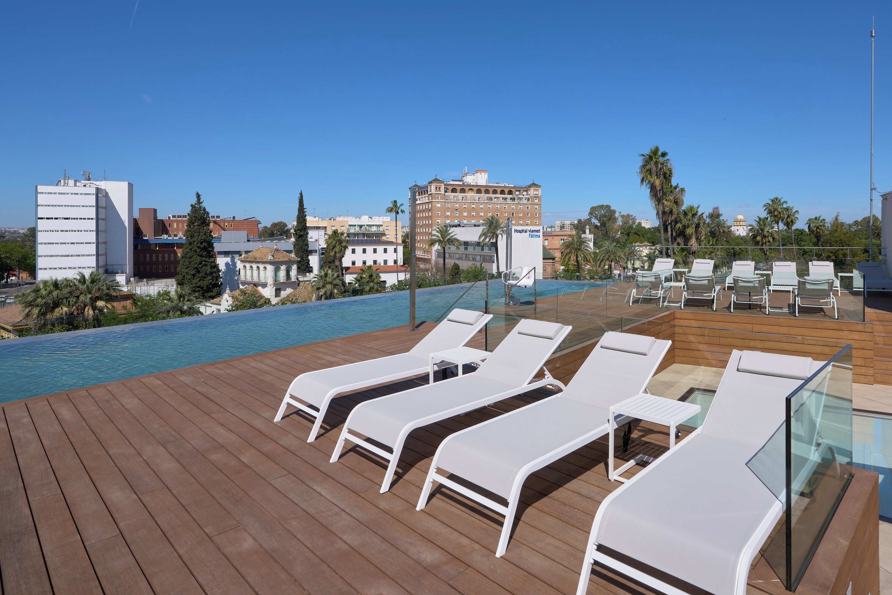 A rooftop pool area with lounge chairs and a view of the cityscape.