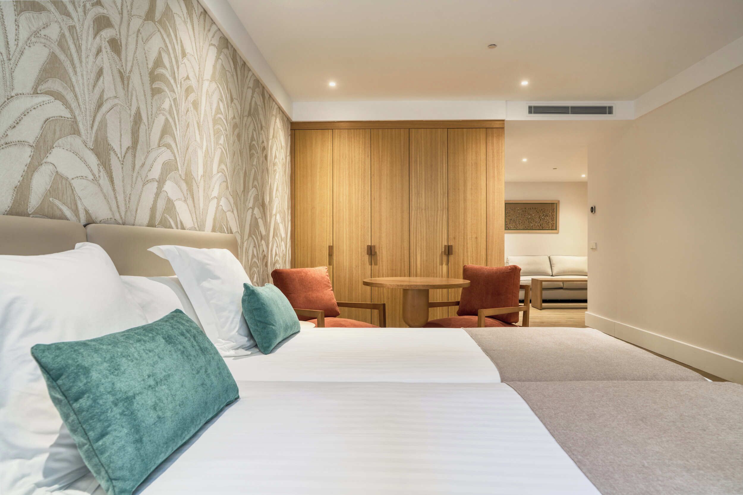 A hotel room with a large bed, a small round table, two chairs, and a wooden wardrobe.
