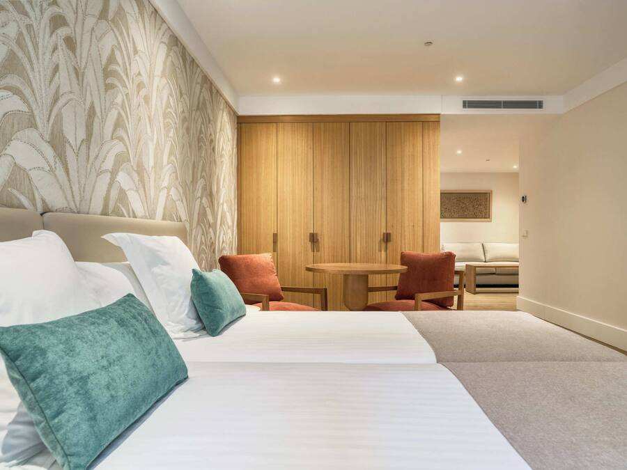 A hotel room with a large bed, a small round table, two chairs, and a wooden wardrobe.