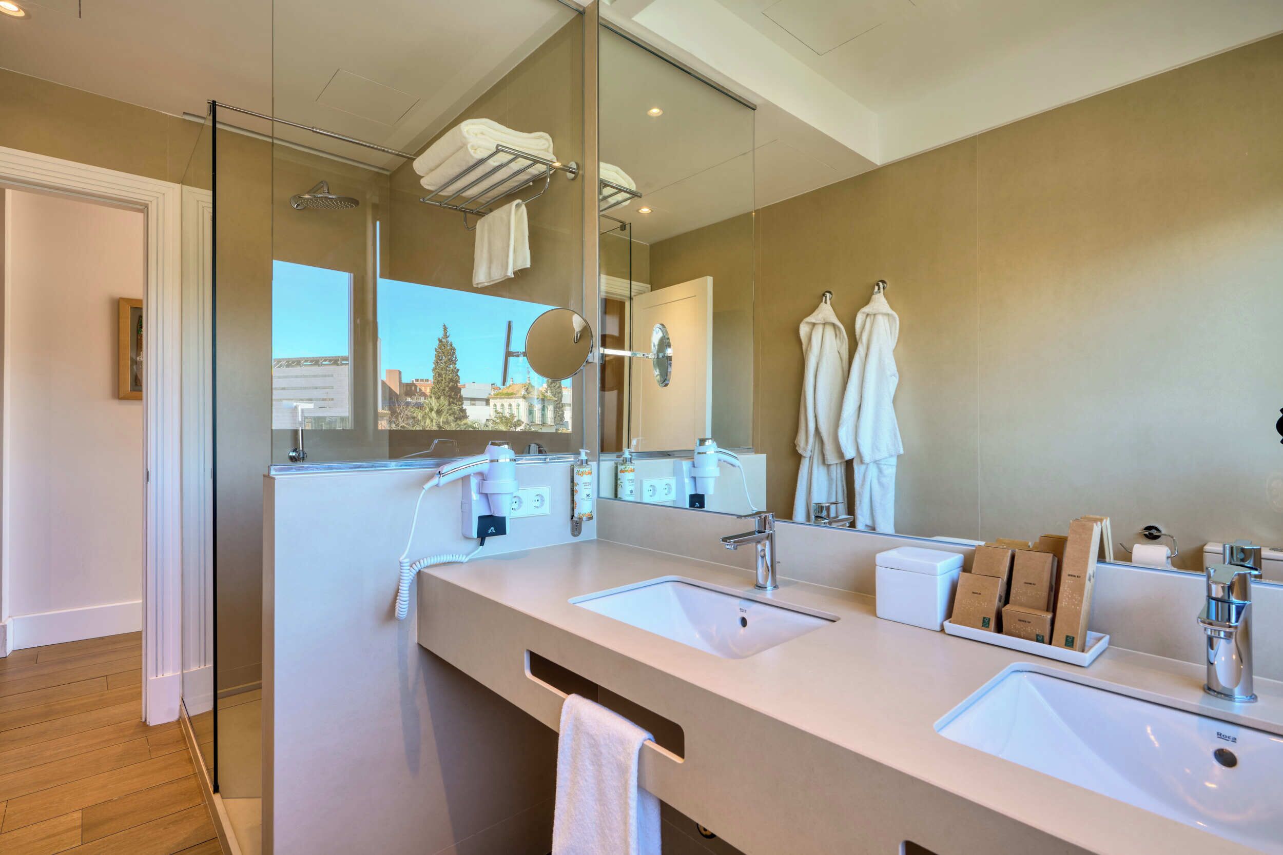A modern bathroom with two sinks, a large mirror, and a view of a building outside.