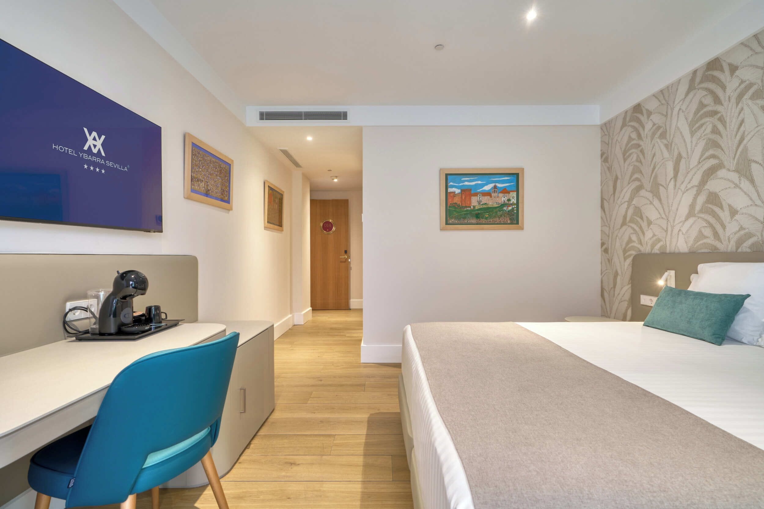 Habitación de hotel con cama, escritorio, silla y un cuadro en la pared.