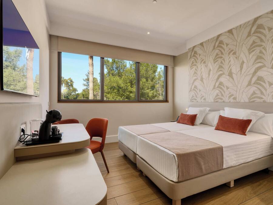 Una habitación de hotel moderna con una cama grande, un escritorio con silla y una ventana con vistas a árboles.