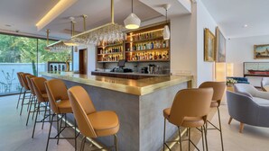 A modern bar area with a bar counter, multiple stools, and a wine rack. - Hotel Ybarra Sevilla (Seville)