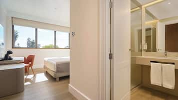 Una habitación de hotel moderna con cama, escritorio, silla y un baño grande con espejo y toallero.