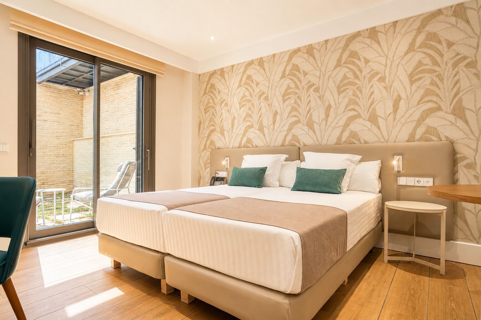 A double bed with a headboard, a bedside table, a chair, and a view of an outdoor patio.