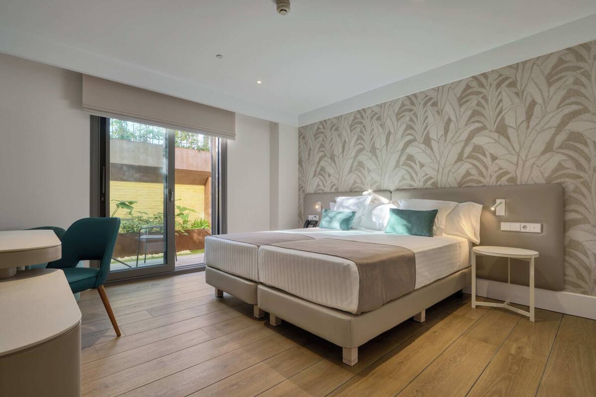 A modern bedroom with a bed, a chair, a small table, and a view of the outdoors.
