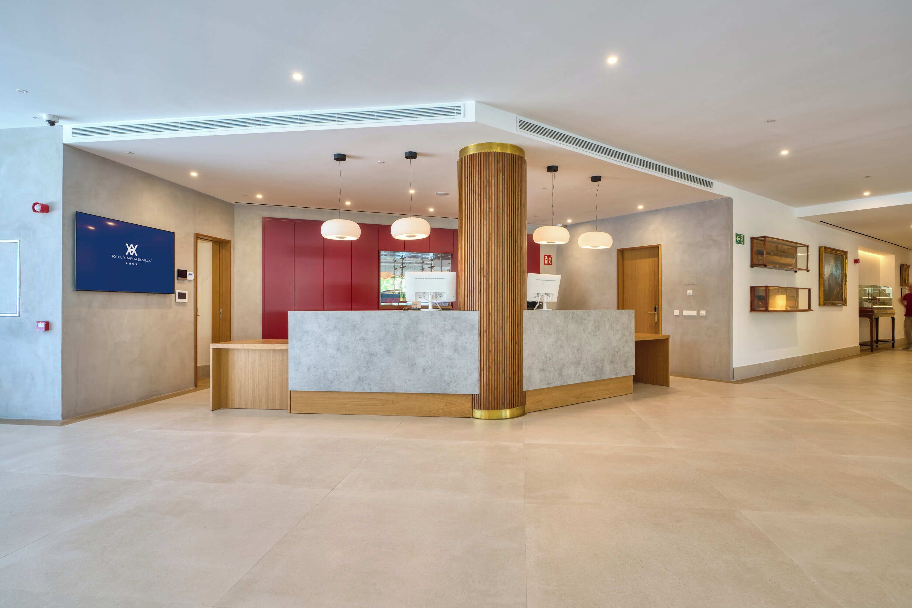 A hotel reception area with a modern design, featuring a reception desk, a large pillar, and pendant lighting.