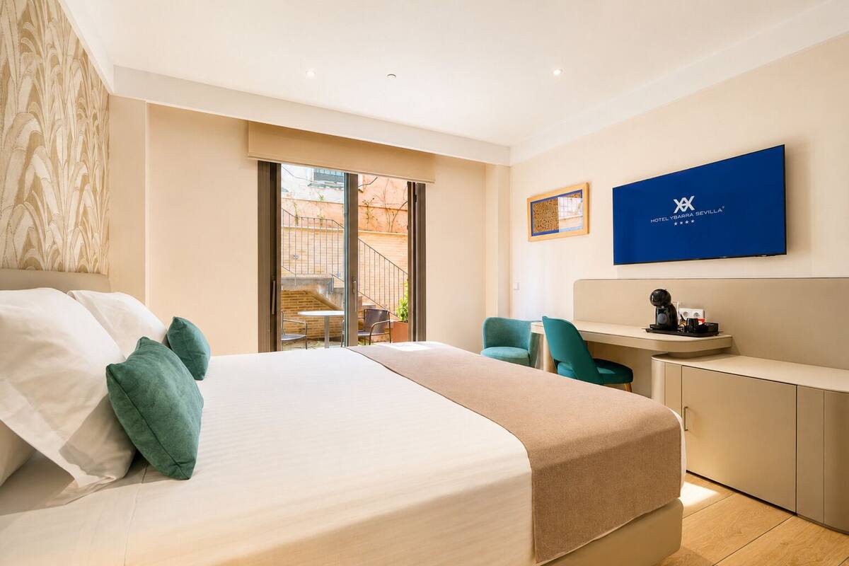 A hotel room with a bed, a desk, a chair, a TV, and a balcony.