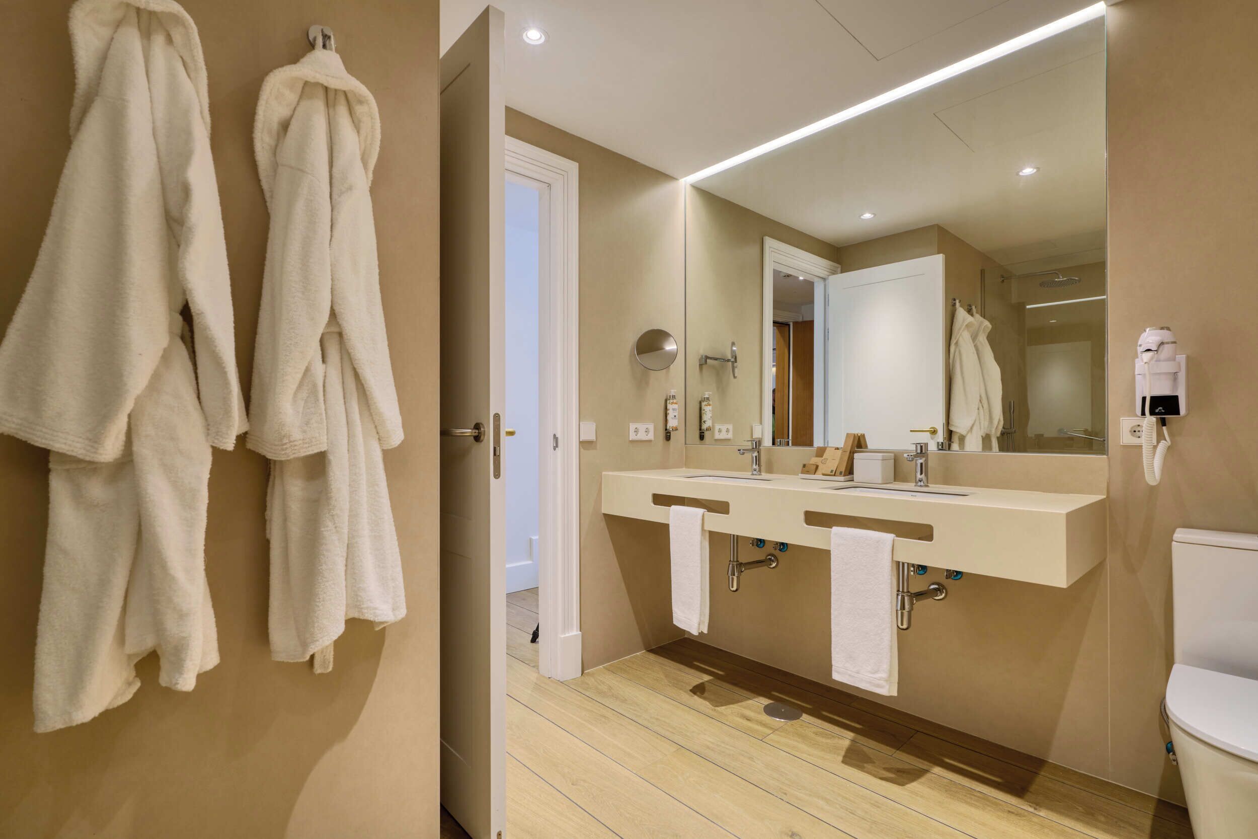Een moderne badkamer met twee wastafels, een spiegel en handdoeken aan de muur.