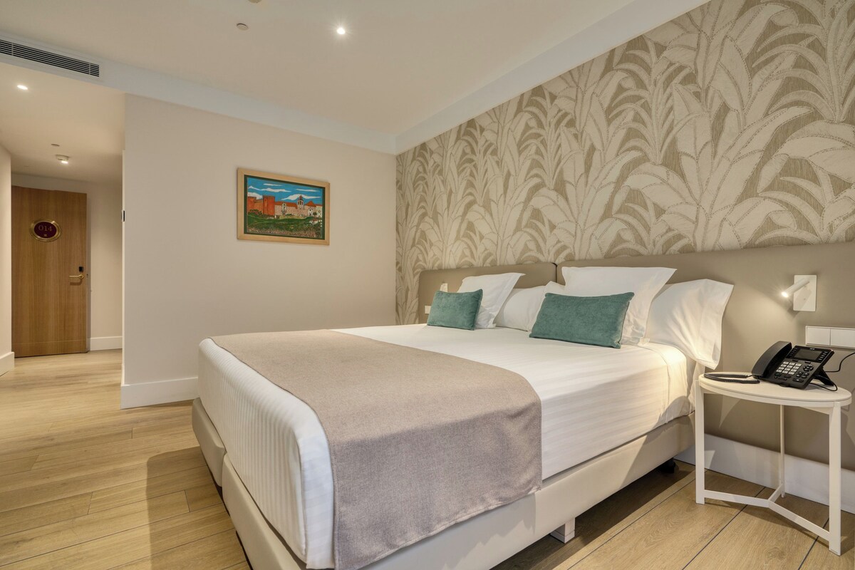 A hotel room with a bed, bedside table with a phone, and a painting on the wall.
