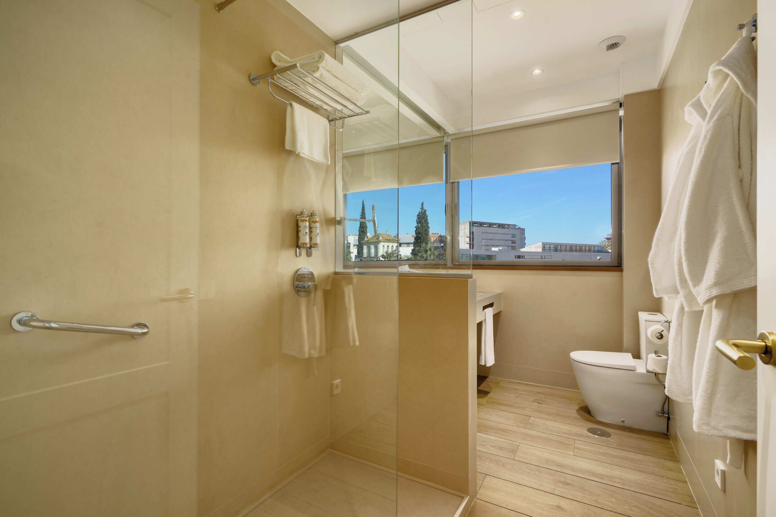 Une salle de bain moderne dotée d’une douche à parois de verre, de toilettes et d’une fenêtre donnant sur la ville.