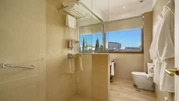 Un baño moderno con cabina de ducha de vidrio, inodoro y ventana con vista a la ciudad.