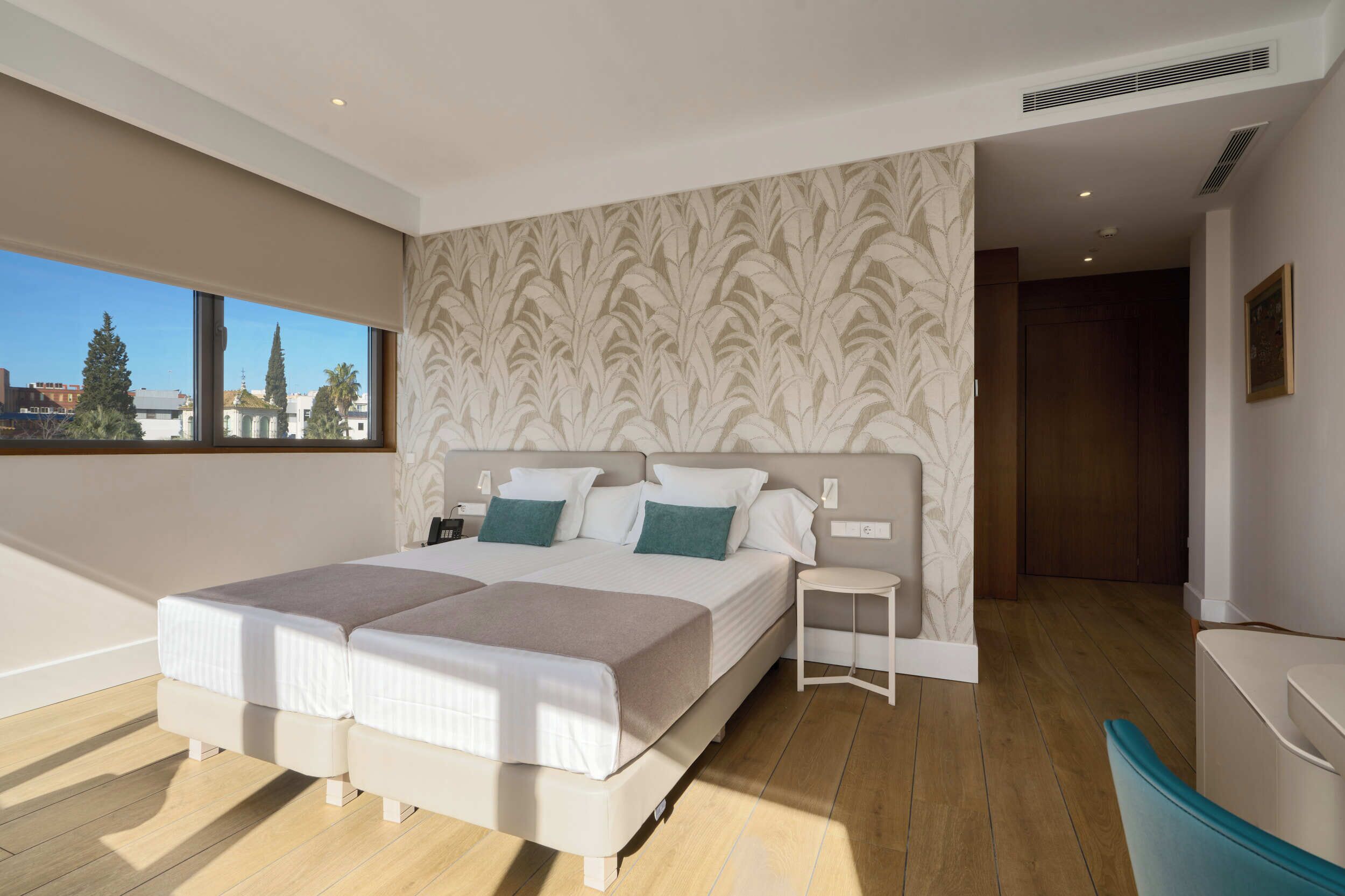 A modern bedroom with a large bed, a small bedside table, a view of the city, and a bathroom with a bathtub.