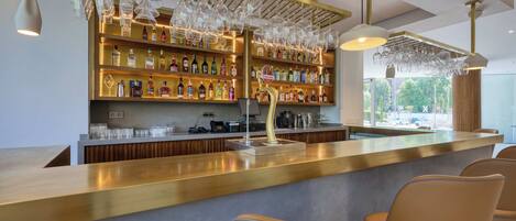 A bar area with a counter, shelves of liquor bottles, and hanging glasses.