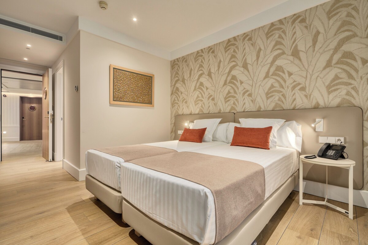 A double bed with a headboard, a bedside table with a phone, and a wall with a patterned wallpaper.
