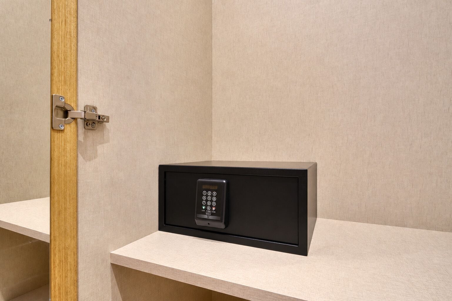 Una habitación con una caja fuerte empotrada en una pared de color claro, una puerta de madera y un suelo de tonos claros.
