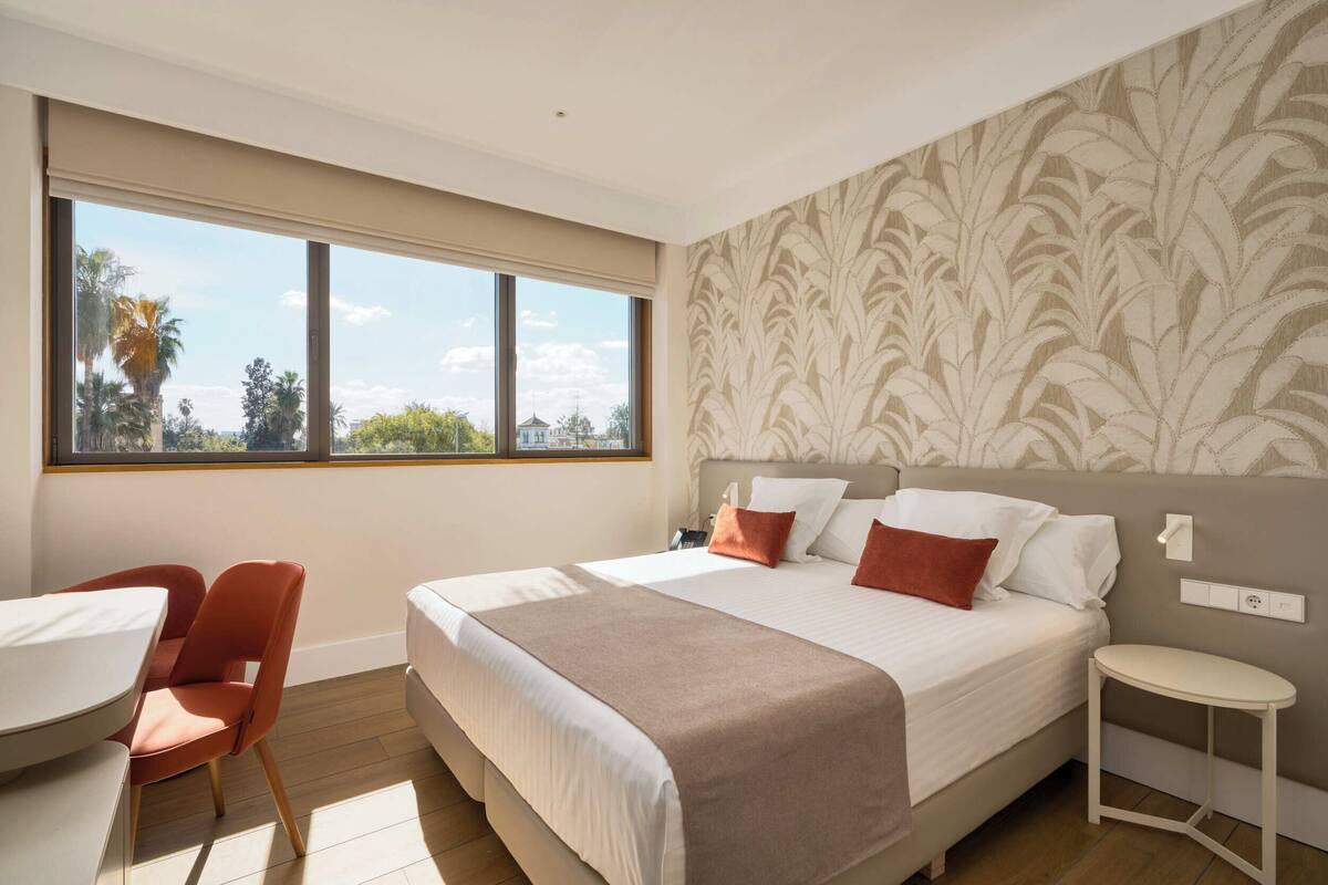 A bedroom with a large bed, a desk, a chair, and a small table.