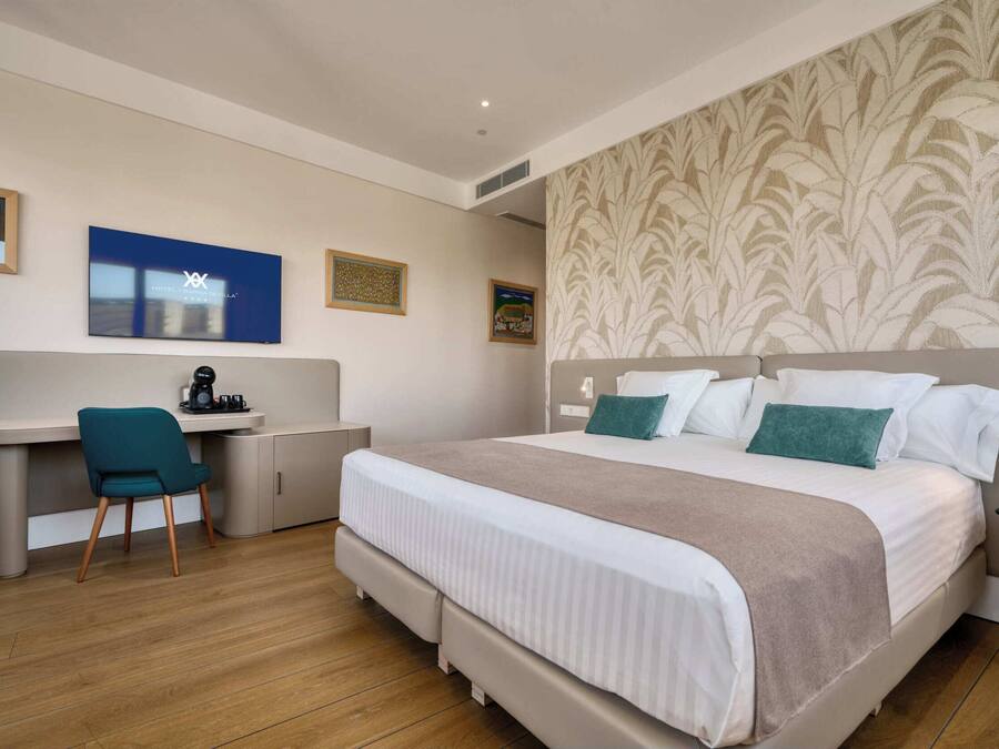 A hotel room with a bed, a desk, a chair, and a television.